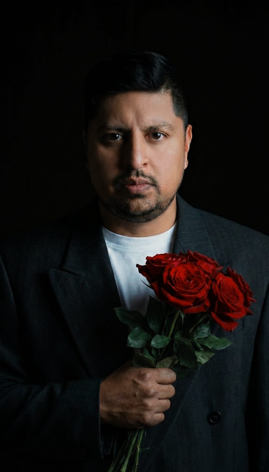 Low-key studio portrait of a man in a pinstripe suit holding red roses