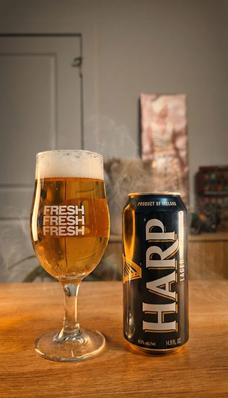 Product photograph of a lager can beside a poured glass on a wooden table
